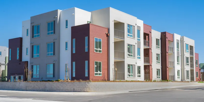 Edificio residencial moderno de varias plantas con fachadas en tonos blanco y granate, junto a una calle.
