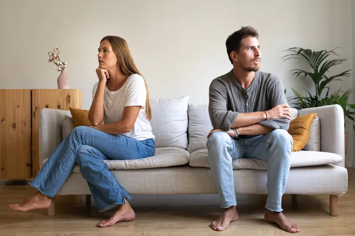 Pareja sentada en un sofá mirando en direcciones opuestas, mostrando distanciamiento y falta de comunicación en la relación